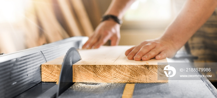 Worker hands details of wood cutter machine with a circular saw and wooden board. Circular cutting s