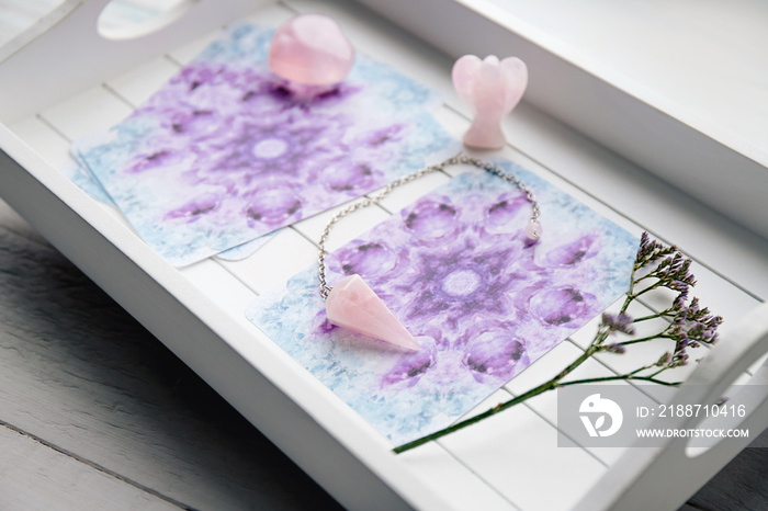 Deck with homemade Angel cards on white tray at home table, surrounded with semi precious stones rose quartz crystals and angel shape figurine.