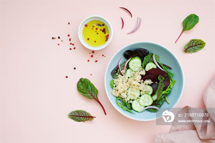 Beetroot salad with quinoa, cucumber, various lettuce leaves and onions on pastel pink background