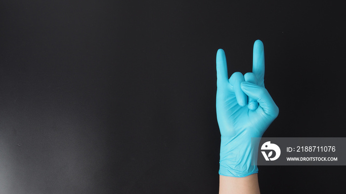 Hand is wear blue glove and doing rock hand sign on black background.