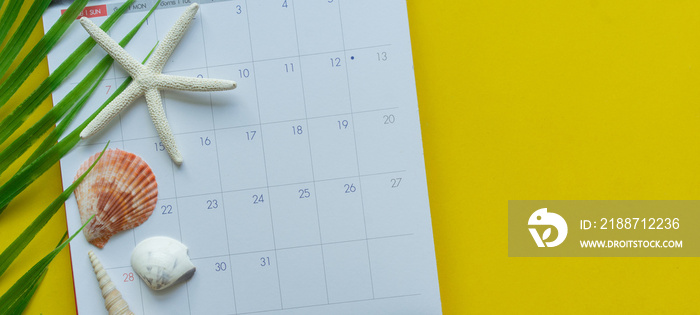 close up top view on white calendar and tropical leaves and shells on yellow table background for planning work and life balance in holiday summer concept