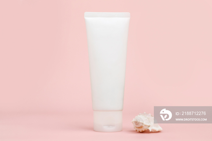 Front view of unbranded white squeeze bottle cream tube and seashell on pink background. Cosmetics with calcium and sea salt. Mockup, template, closeup.