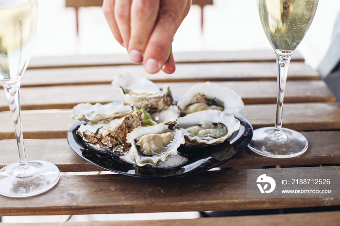 Squeezing lime on oysters. Two glasses of sparkling wine on a wooden table in an outdoor cafe