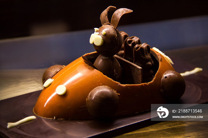 The chocolate rabbit rides in a chocolate car with chocolate bunnies. the cake is in the shop window behind the glass