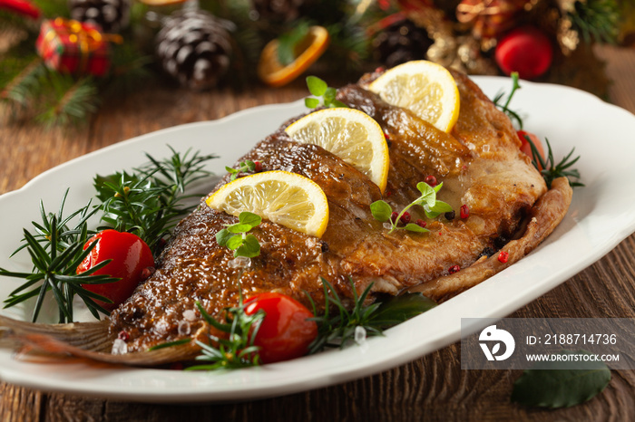 Fried carp whole. Served with lemon and cherry tomatoes on white plate. Christmas decoration.