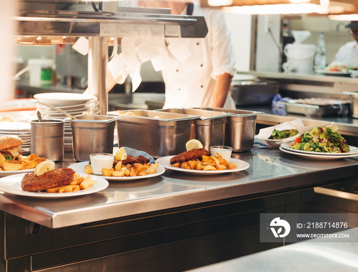 Food orders on the kitchen table in the restaurant, chief decorating schnitzel and fried potatoes, traditional german plate