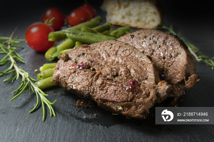 grilled lamb steak with green beans, tomatoes and rosemary on dark slate, close up