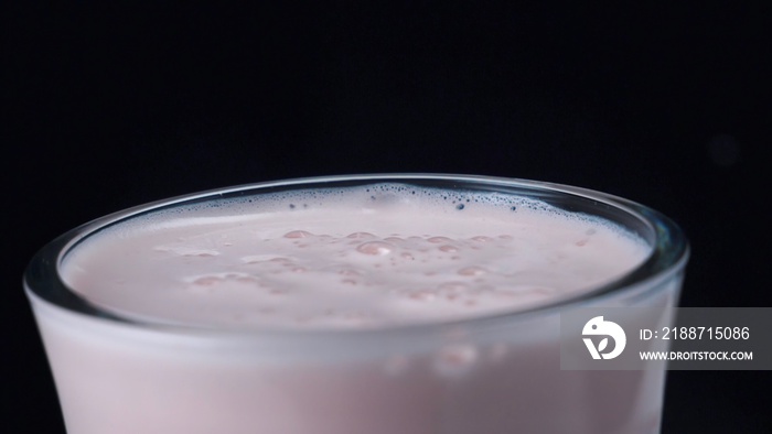 Close-up of delicious milkshake with strawberry falling in the glass. Frame. Isolated on black