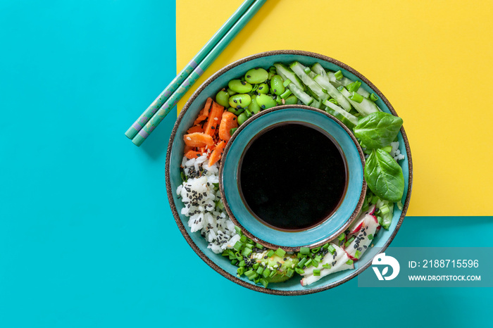 Pan Asian trendy Homemade Vegan Poke Bowl with Rice, edamame, fresh vegetables and soy sauce, served with chopsticks on vivid yellow and turquoise background