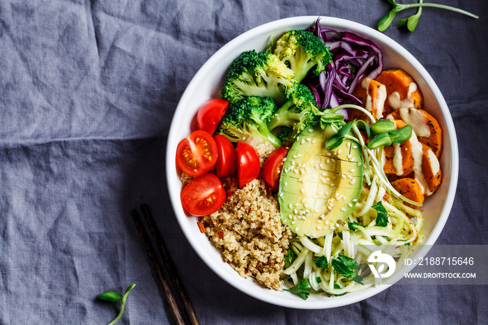 Buddha bowl salad with quinoa, avocado, broccoli, sweet potato and tahini dressing, gray background.