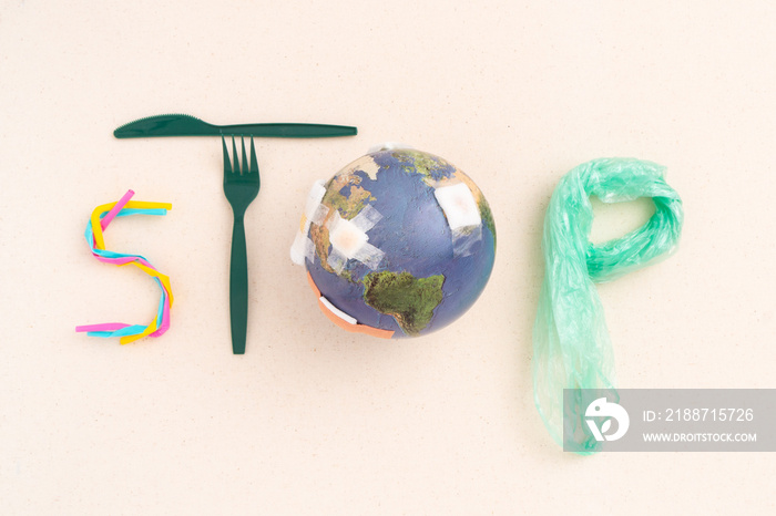 Beautiful flat lay of single use plastic items (drinking straws, grocery bag, single-use cutlery) and globe with bandages arranged into word STOP on canvas for global warming, climate change campaign.