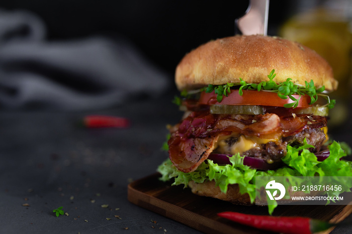 Fresh burger with red hot chili pepper on wooden desk on dark background. Hot Hamburger with bacon, beef meat, tomato, spicy sauce and lettuce on dark mood style