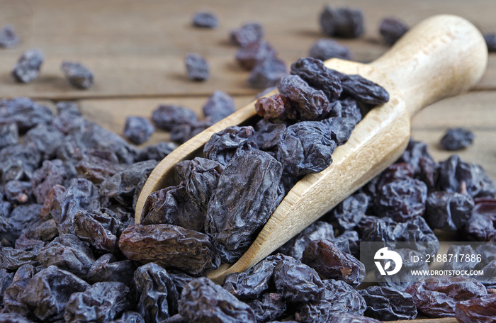 black raisins in a scoop on a wooden table. heap of black raisins close up.