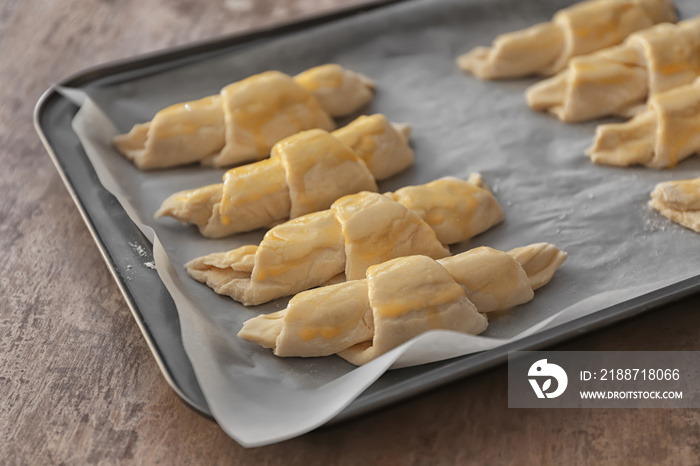 Baking sheet with raw croissants on table, closeup