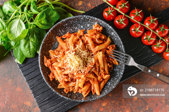 Bowl of penne pasta with tomato sauce on color background