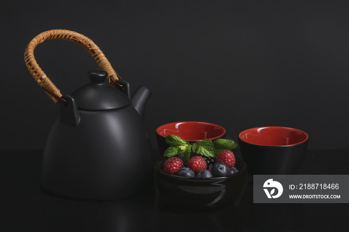 Items for tea on the table, black and red cups with black-red berries.