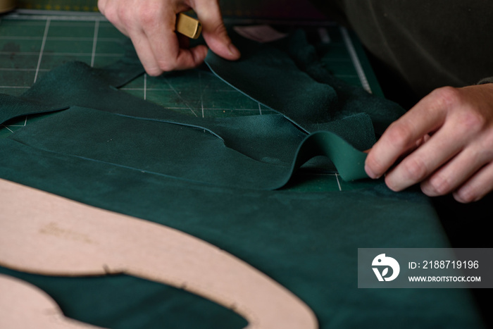 Shoemaker cutting suede leather with craft knife for handmade shoes in workshop. Making bespoke shoes. Closeup.