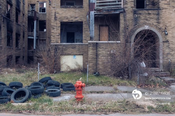 Red fire hydrant in front of abandoned building with forgotten tires and overgrown brush