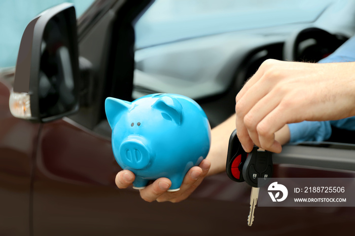 Man holding piggy bank and key in his new car