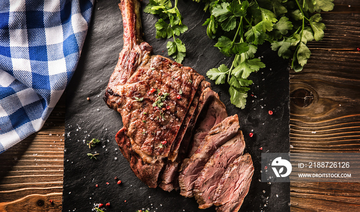 Freshly grilled tomahawk steak on slate plate with salt pepper rosemary and parsley herbs. Sliced pieces of juicy beef steak