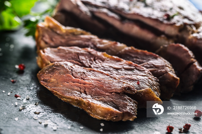 Freshly grilled beef steak on slate plate with salt pepper rosemary and parsley herbs. Sliced pieces of juicy beef steak