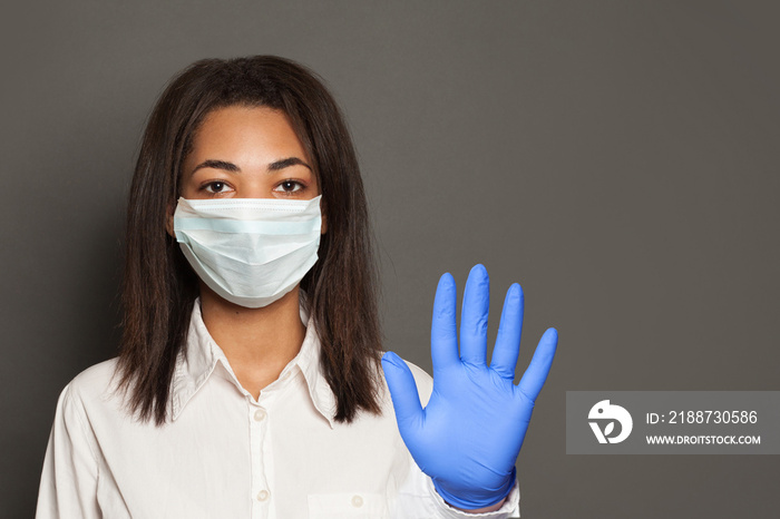 Woman doctor or scientist in a medical face mask showing stop pandemic gesture. Black woman in safety mask and medical gloves