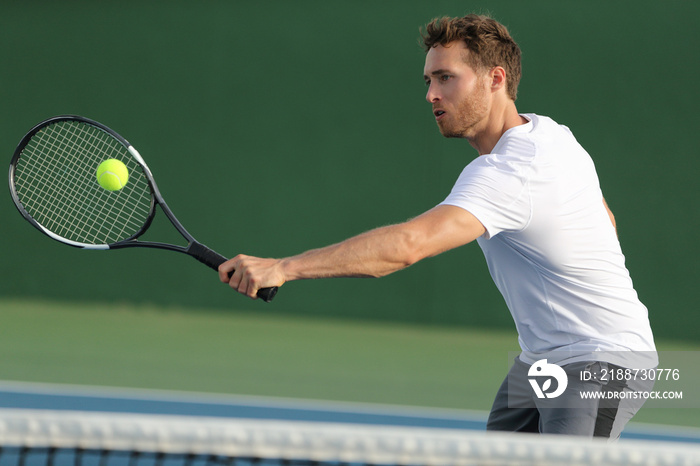 Tennis player hitting ball with backhand racket on hard court. Man playing game returning ball portrait.