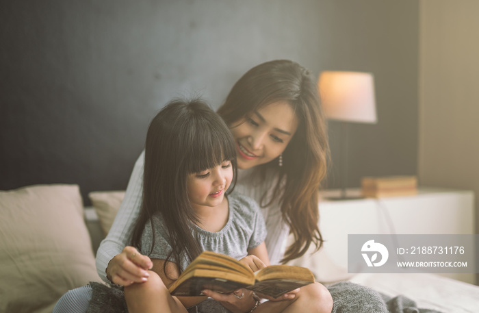 mother and daughter reading book at home in the bedroom