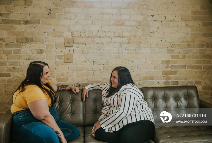 2 women sit on sofa and talk