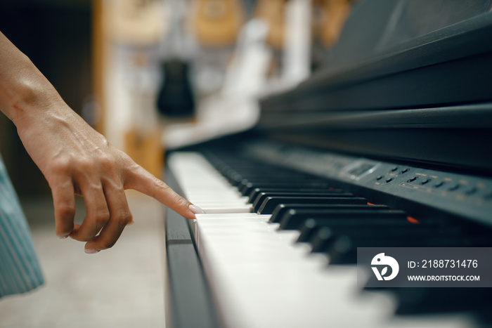 Young woman choosing digital piano in music store