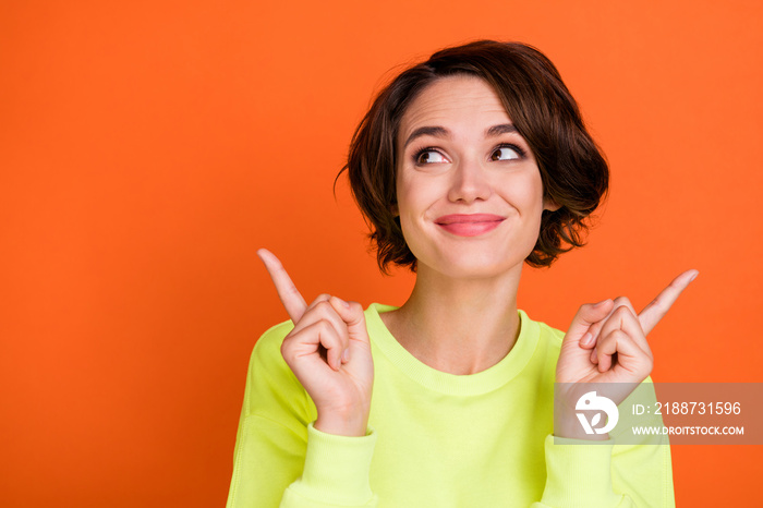 Photo of young happy dreamy pretty woman point fingers look empty space smile isolated on orange color background