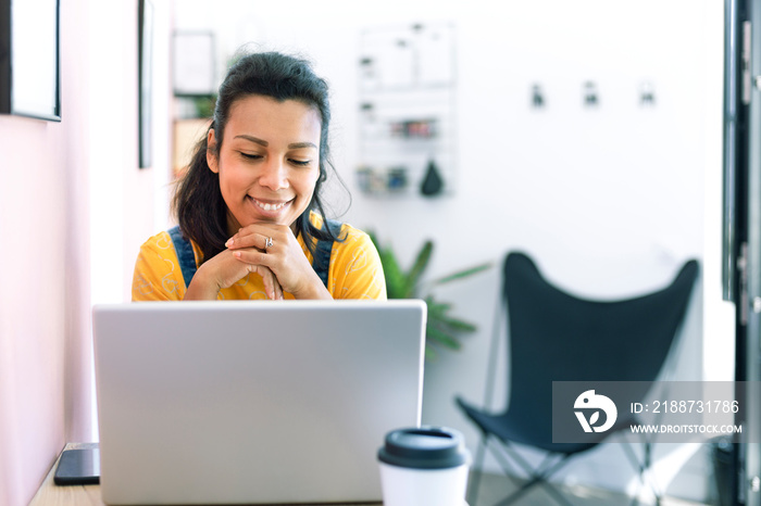 Young latina woman using a laptop at her workplace. Space for text.