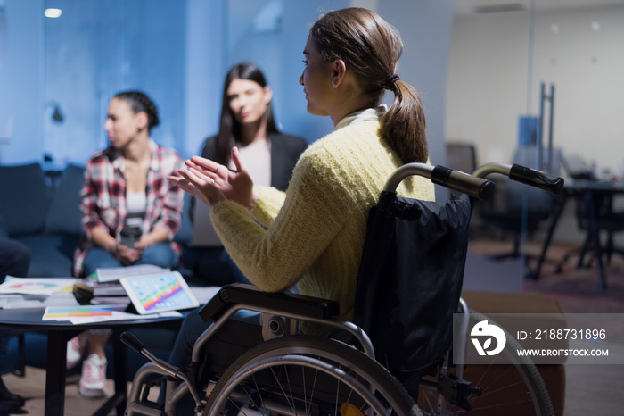 Handicapped young woman with colleagues working in office. She is smiling and passionate about the workflow. Performing in co-working space. Office people working together.