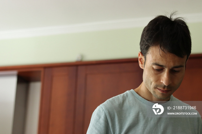 Thoughtful brown man in green t-shirt looking down indoors. Copy space.