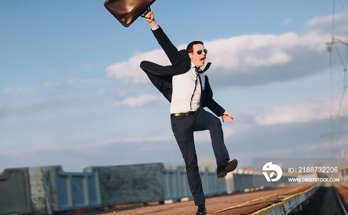 The joy of success. Young lucky businessman on railway platform.Businessman in suit happily runs and throws his suitcase.