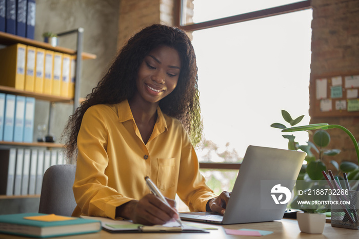 Portrait of happy afro american young businesswoman write note work laptop consultant indoors in office workplace