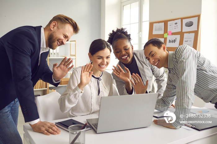 Group of mixed race office workers having online video conference meeting with international colleagues. Team of happy diverse business people waving hands at laptop computer saying hello to coworkers