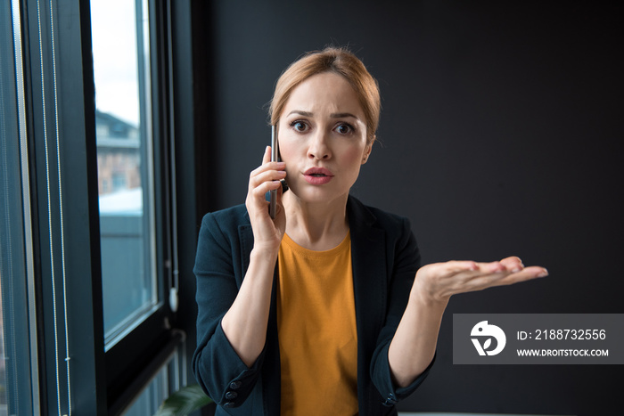 Portrait of surprised girl talking by phone while flourishing arm. Business and conversation concept