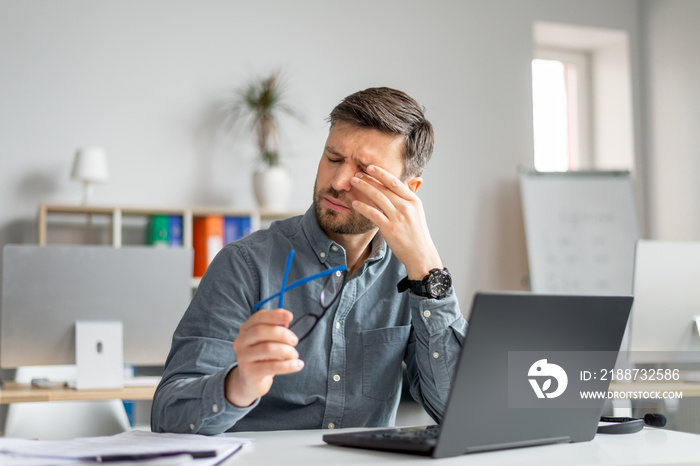 Tired mature man feeling pain eye strain, rubbing dry irritated eyes, fatigued from computer work, sitting in office