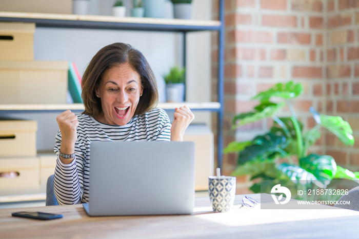 Middle age senior woman sitting at the table at home working using computer laptop screaming proud and celebrating victory and success very excited, cheering emotion