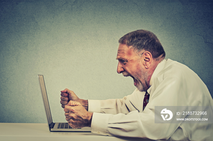 Angry furious senior business man working on computer, screaming