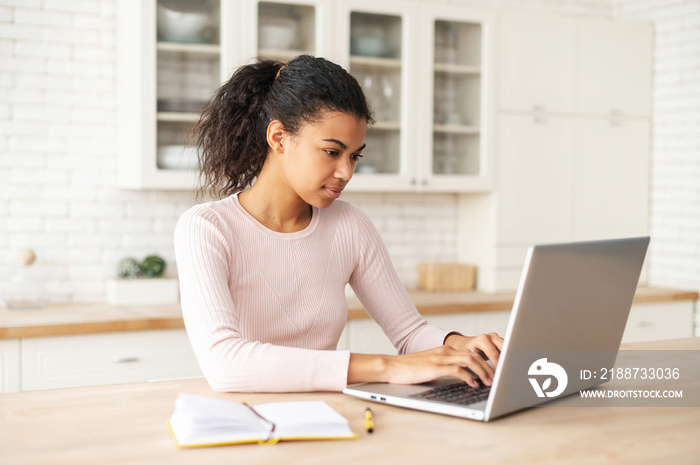 Successful businesswoman with curly ponytail, typing an e-mail on laptop at home office, working remotely, by the tabletop, checking her plans, freelancer, discussing a new project with team