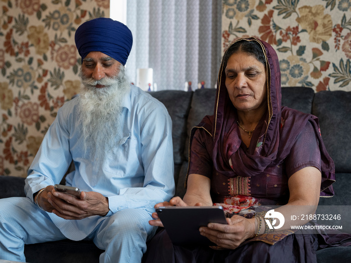 Senior couple in traditional clothing using phone and tablet at home