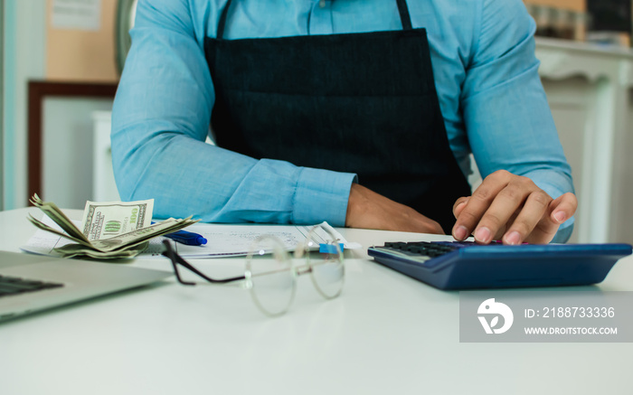 Selective focus on accounting man hand using calculator, calculating income, budget, profit with dollar bank notes after selling food and beverage in own cafe and restaurant.