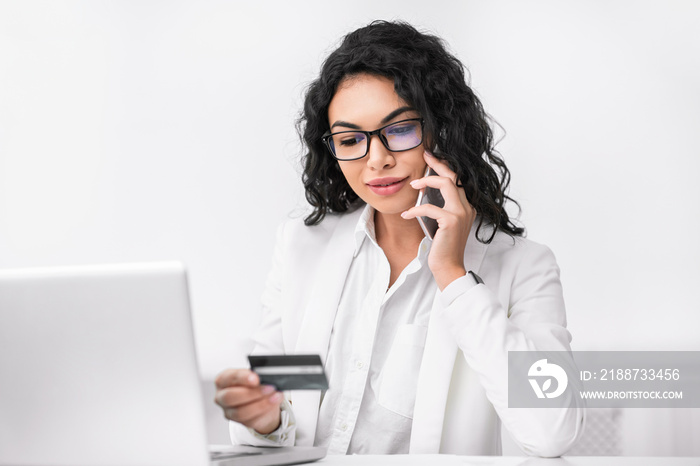 Latin woman holding credit card talking on phone