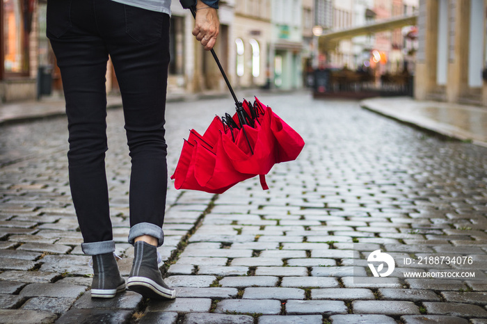 Woman holding leather bag and red umbrella and she is walking on the street after rain