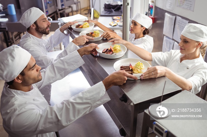 Chefs passing ready food to waiter at order station