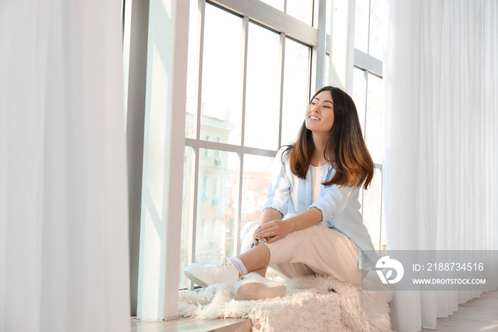 Pretty young Asian woman sitting on window sill