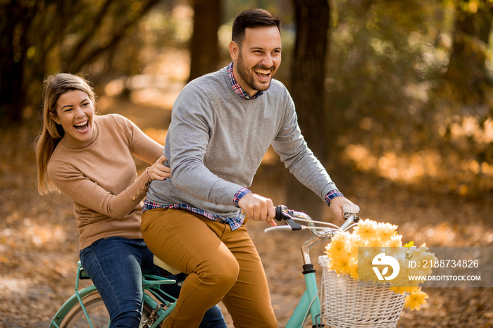 Active young couple enjoying together in riding bicycle in golden autumn park