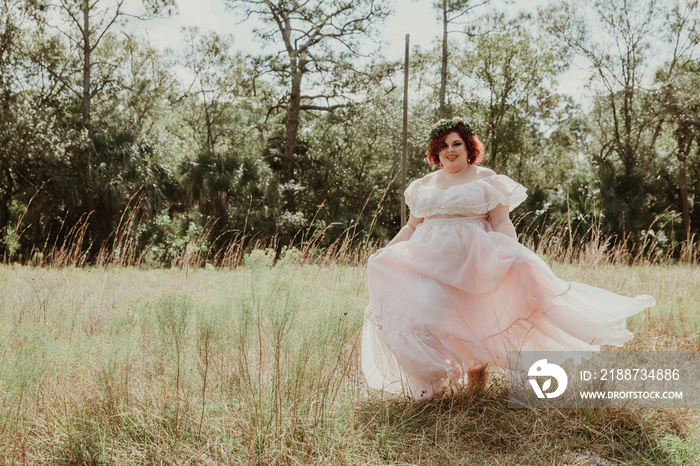 plus size woman runs through field in pink dress